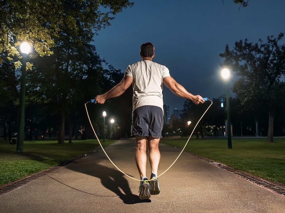 夜の公園で縄跳びをしている男性のバックショット